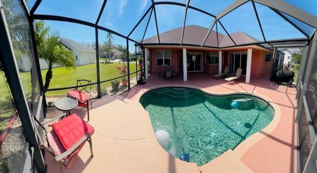 outdoor pool with glass enclosure, a patio, and a lawn