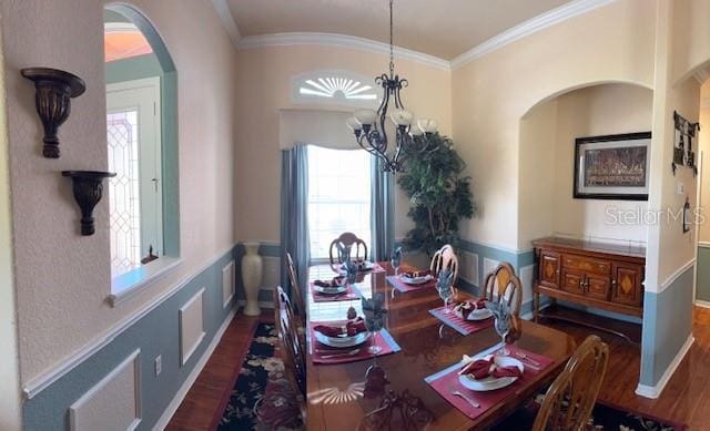 dining area featuring a chandelier, arched walkways, wood finished floors, and ornamental molding