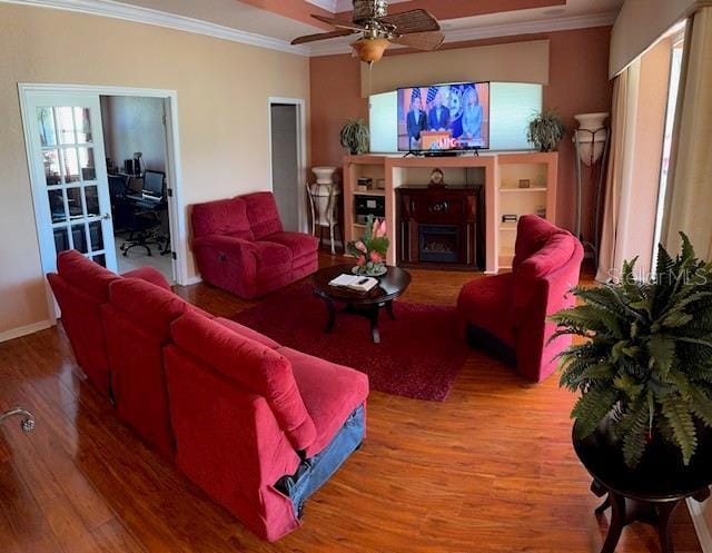 living area with crown molding, baseboards, ceiling fan, a fireplace, and wood finished floors