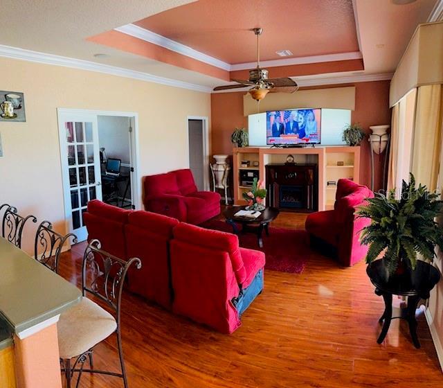 living room with ornamental molding, a fireplace, wood finished floors, a raised ceiling, and a ceiling fan