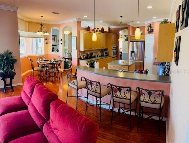 kitchen with wood finished floors, visible vents, ornamental molding, appliances with stainless steel finishes, and pendant lighting