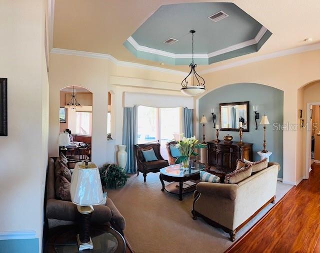 living area with a tray ceiling, visible vents, arched walkways, and ornamental molding