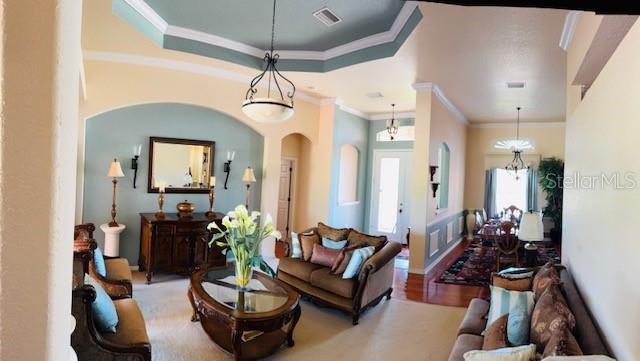 living area with visible vents, crown molding, wood finished floors, arched walkways, and a raised ceiling