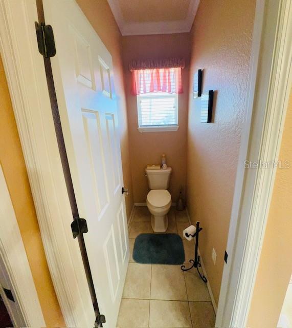 bathroom with baseboards, toilet, crown molding, and tile patterned flooring