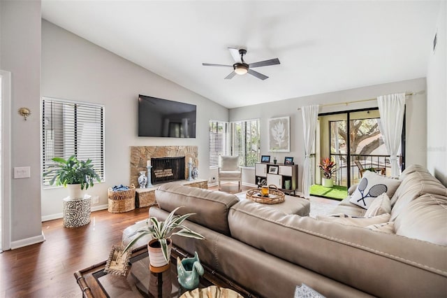 living area with baseboards, ceiling fan, lofted ceiling, a stone fireplace, and wood finished floors