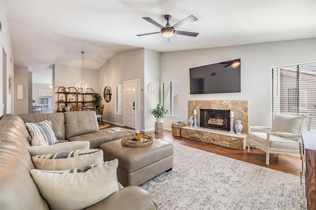 living room with wood finished floors, baseboards, lofted ceiling, a fireplace, and ceiling fan with notable chandelier