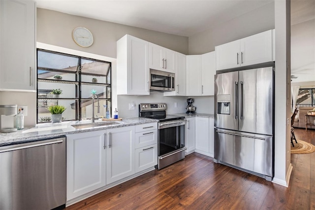 kitchen featuring a sink, light stone counters, appliances with stainless steel finishes, and dark wood finished floors