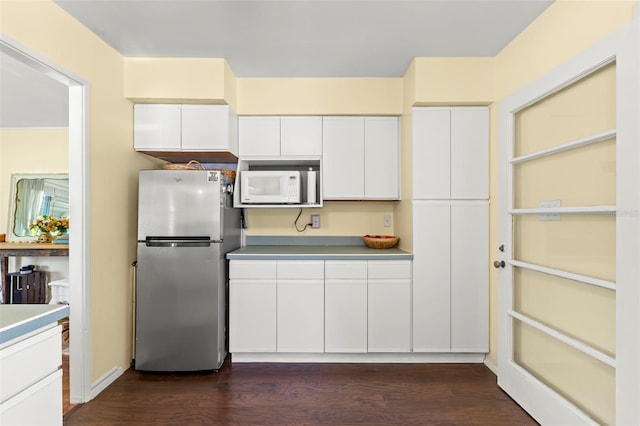 kitchen featuring white cabinetry, dark wood-type flooring, white microwave, and freestanding refrigerator