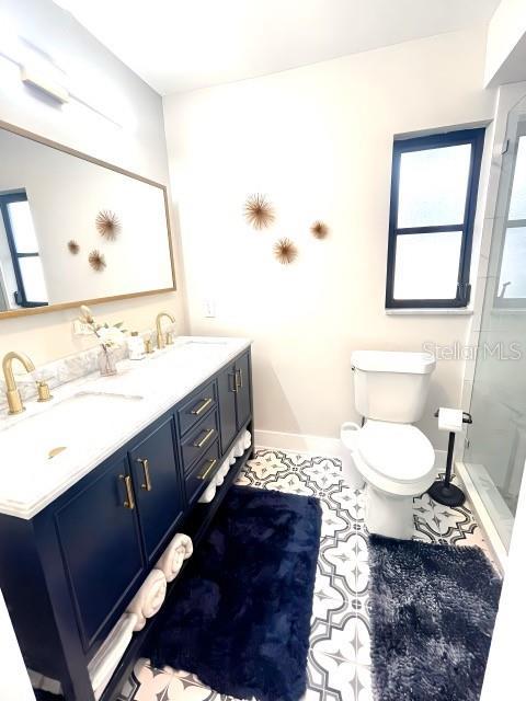 full bath featuring a sink, baseboards, toilet, and a stall shower