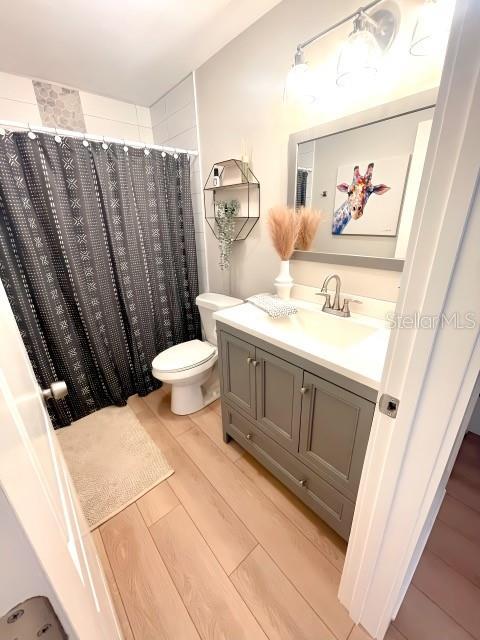 full bathroom with a shower with curtain, toilet, wood finished floors, and vanity