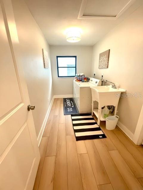 interior space with washing machine and clothes dryer, a sink, baseboards, and wood finished floors