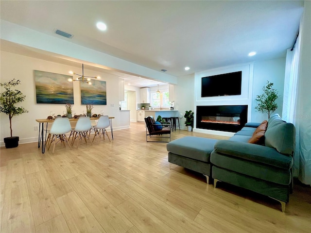 living area featuring light wood finished floors, visible vents, baseboards, recessed lighting, and a glass covered fireplace