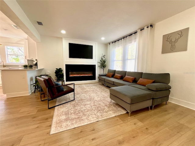 living room featuring light wood finished floors, visible vents, baseboards, recessed lighting, and a glass covered fireplace