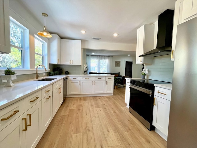 kitchen with light wood finished floors, visible vents, stainless steel appliances, wall chimney exhaust hood, and a sink