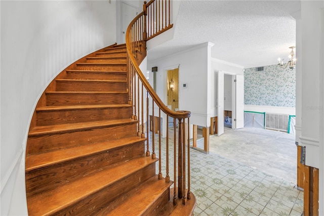 stairway featuring visible vents, wallpapered walls, a chandelier, wainscoting, and a textured ceiling