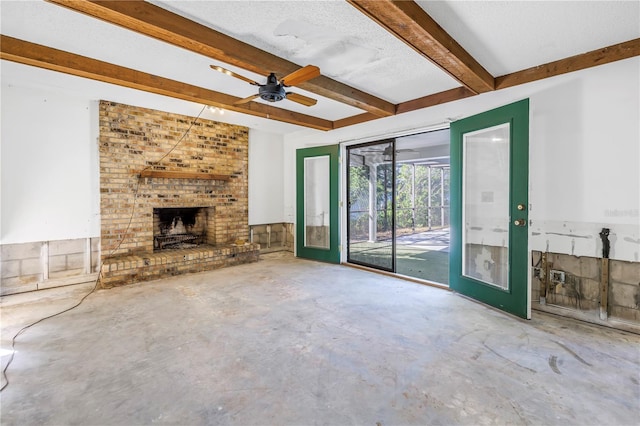 unfurnished living room with a brick fireplace, beamed ceiling, concrete flooring, a textured ceiling, and a ceiling fan