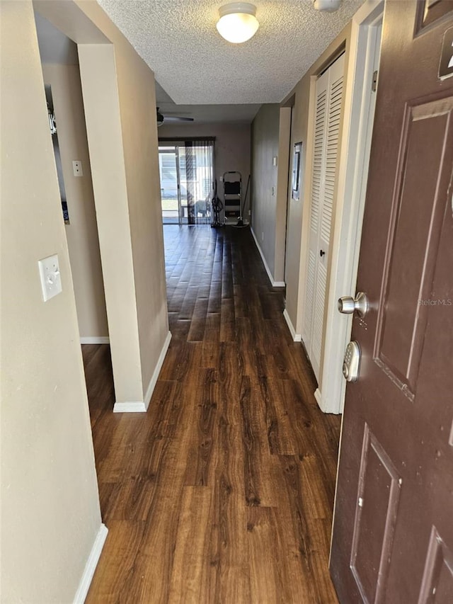 hallway with a textured ceiling, baseboards, and wood finished floors