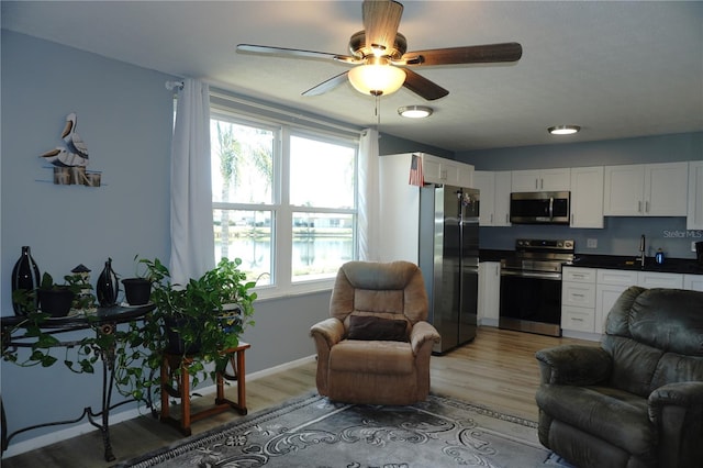 interior space featuring a sink, open floor plan, stainless steel appliances, light wood finished floors, and ceiling fan