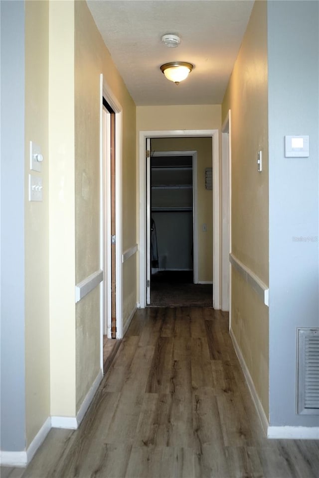 corridor featuring visible vents, baseboards, and wood finished floors