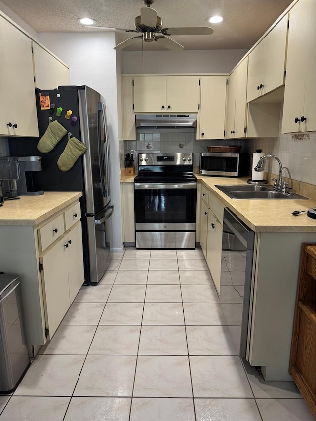 kitchen featuring a ceiling fan, a sink, stainless steel appliances, under cabinet range hood, and tasteful backsplash