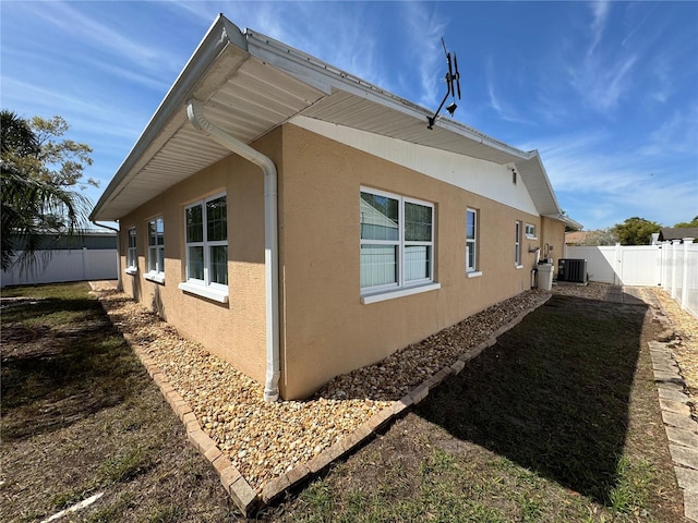 view of side of property with a fenced backyard, stucco siding, and central AC