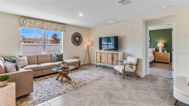 living room with light tile patterned floors, visible vents, a textured ceiling, and baseboards