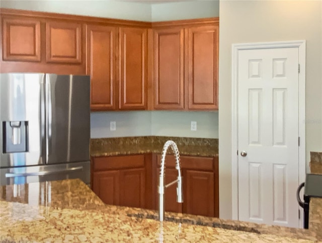 kitchen featuring light stone counters, stainless steel fridge, and brown cabinets