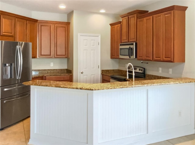 kitchen featuring brown cabinets, appliances with stainless steel finishes, a peninsula, and light stone countertops