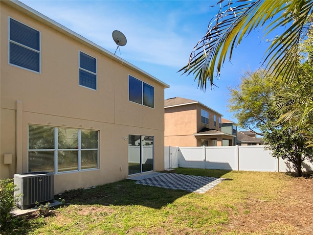 rear view of house featuring a yard, fence, central AC, and stucco siding