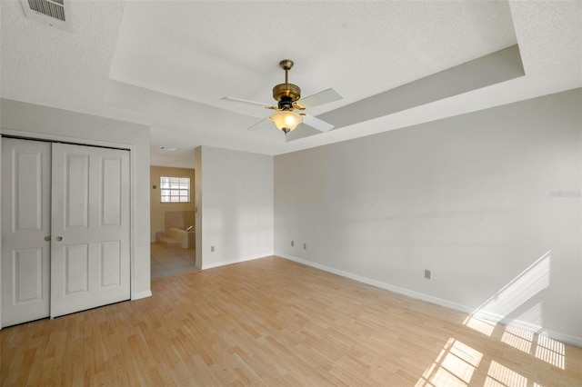 5014 Sterling Manor Dr, Tampa, FL 33647 - unfurnished bedroom featuring baseboards, light wood-type flooring, a tray ceiling, ceiling fan, and a textured ceiling