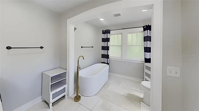 full bathroom with heating unit, visible vents, baseboards, and a freestanding tub