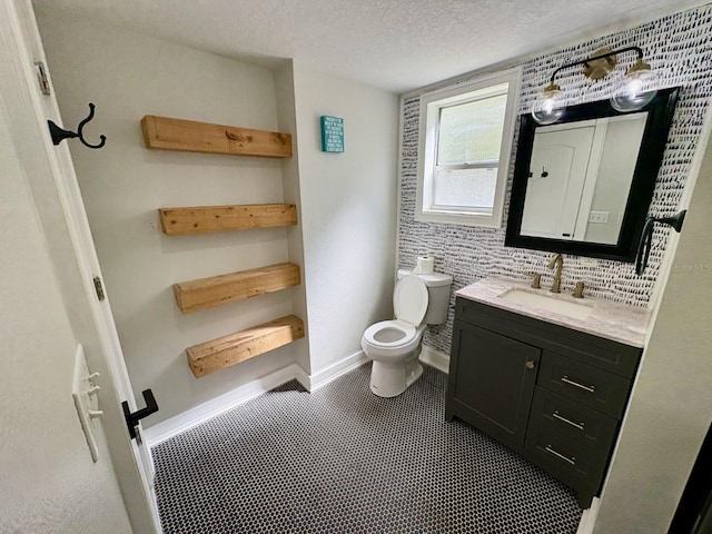 half bathroom with baseboards, a textured ceiling, vanity, and toilet