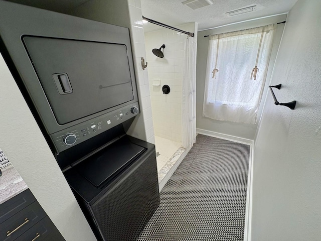 bathroom with visible vents, a textured ceiling, a shower stall, and stacked washer / dryer