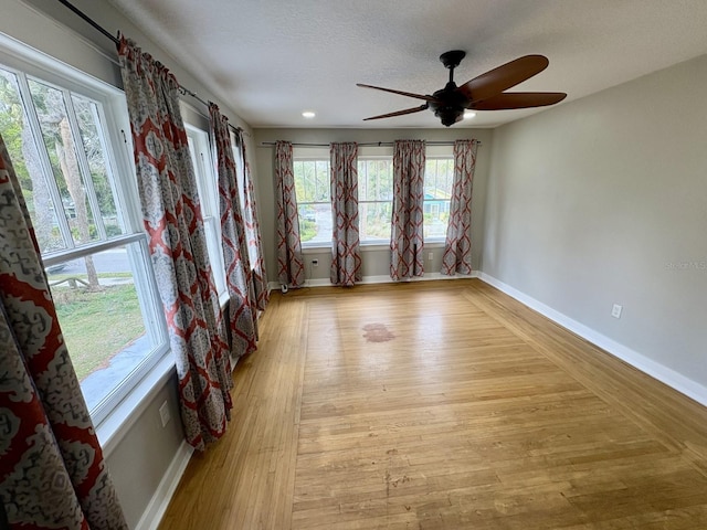 empty room featuring ceiling fan, a textured ceiling, baseboards, and light wood-style floors