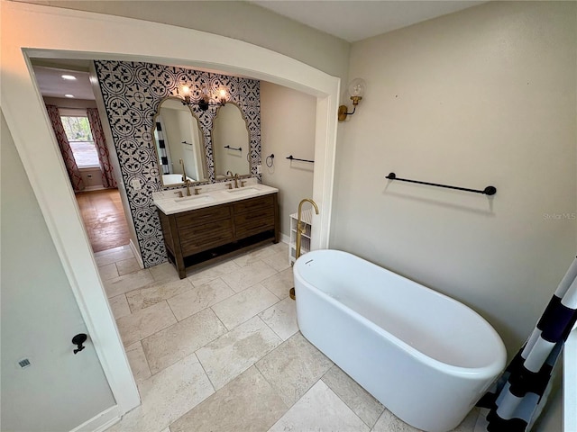 full bathroom featuring a sink, double vanity, baseboards, and a freestanding bath