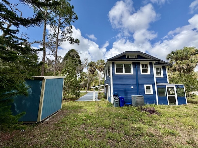 rear view of property featuring an outbuilding, central AC unit, and a lawn