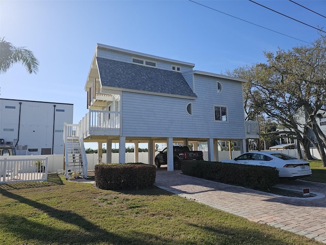 back of house featuring fence, roof with shingles, a yard, a carport, and decorative driveway