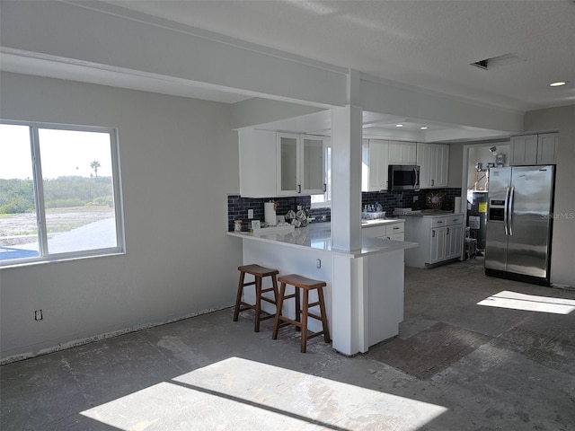 kitchen featuring tasteful backsplash, appliances with stainless steel finishes, a kitchen bar, and a peninsula