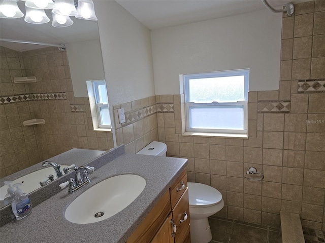 bathroom with tile walls, a wainscoted wall, toilet, a tile shower, and vanity