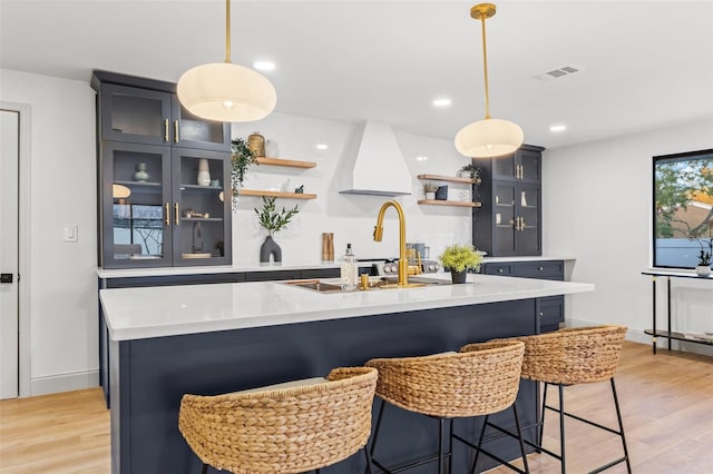 kitchen with visible vents, a center island with sink, open shelves, light wood-style flooring, and light countertops