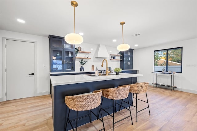 kitchen with a center island with sink, a breakfast bar, light countertops, light wood-style floors, and open shelves