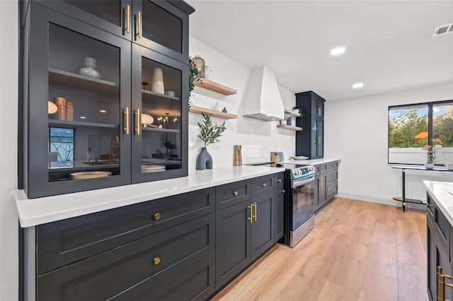 kitchen with custom exhaust hood, light wood-style flooring, open shelves, stainless steel electric range, and light countertops