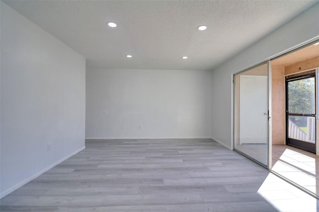 spare room featuring recessed lighting, baseboards, light wood-style floors, and a textured ceiling