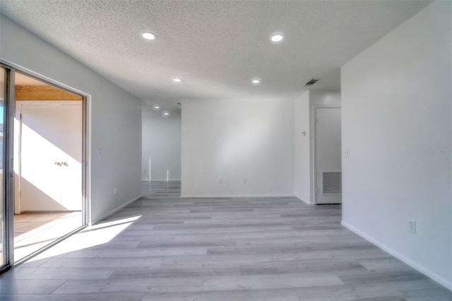 empty room featuring visible vents, a textured ceiling, recessed lighting, light wood finished floors, and baseboards