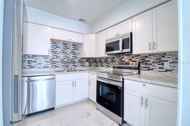 kitchen featuring tasteful backsplash, white cabinets, marble finish floor, stainless steel appliances, and a sink