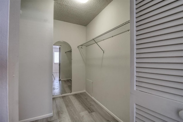 walk in closet with wood finished floors and arched walkways