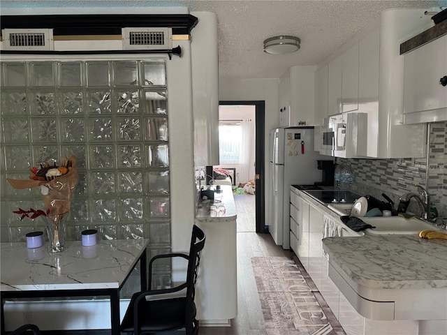 kitchen featuring stainless steel microwave, backsplash, a textured ceiling, white cabinetry, and a sink