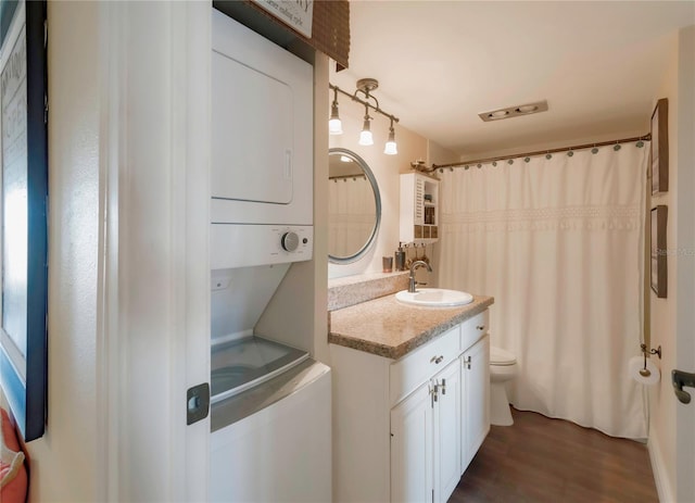 bathroom with curtained shower, toilet, stacked washing maching and dryer, wood finished floors, and vanity