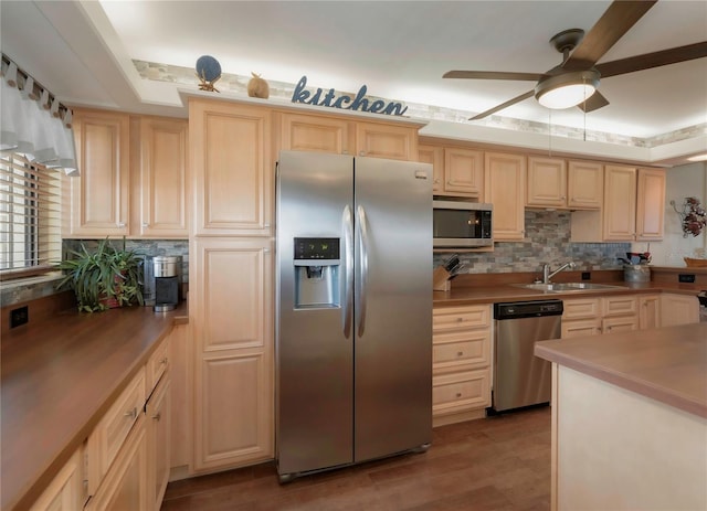 kitchen featuring light brown cabinets, ceiling fan, decorative backsplash, stainless steel appliances, and a sink