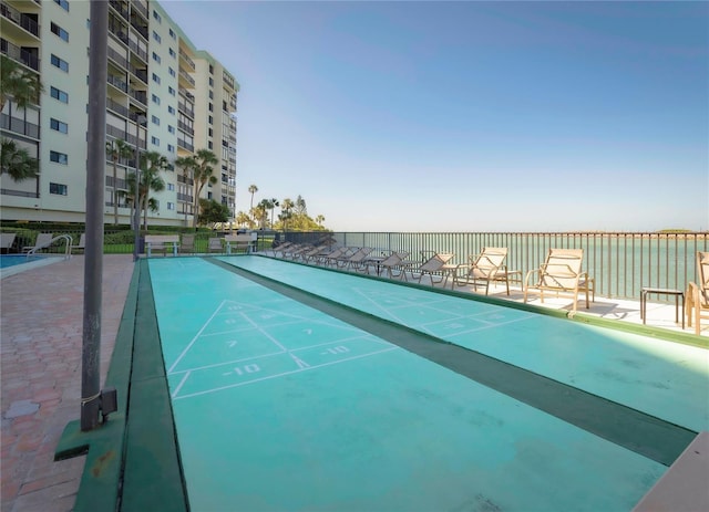 view of property's community with shuffleboard, a water view, and fence